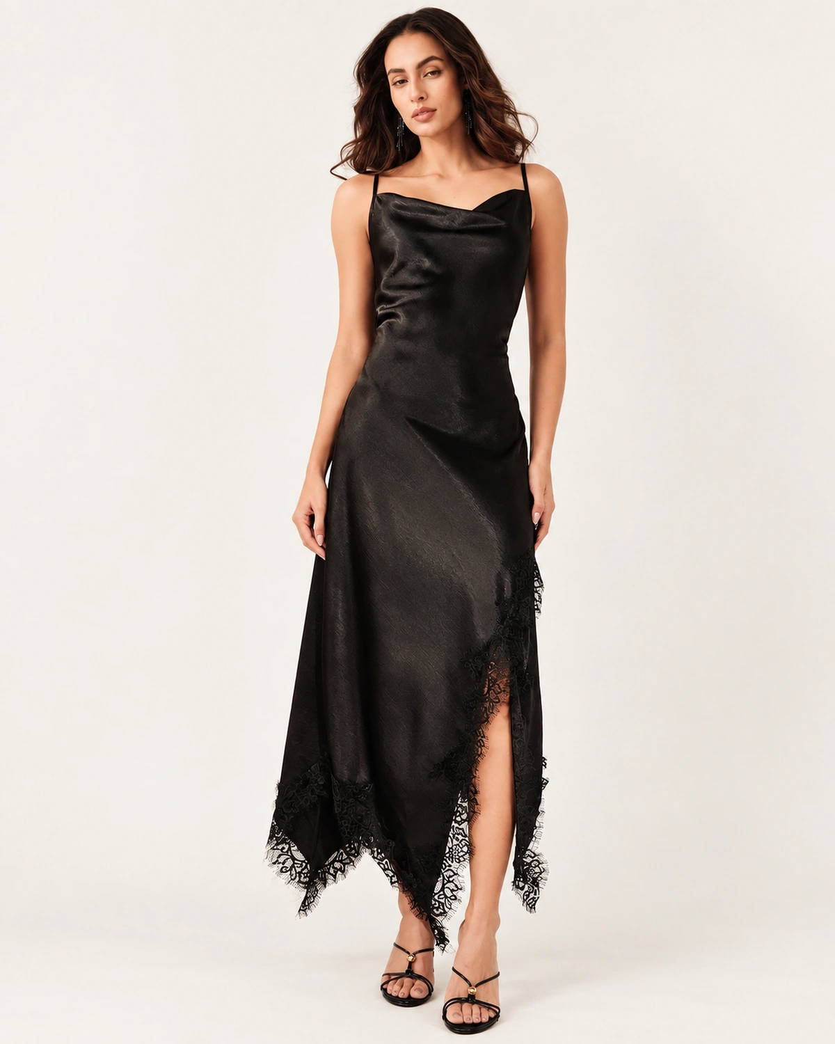 Modelo de corpo inteiro vestindo vestido slip dress midi preto acetinado com fenda lateral e acabamento em renda.