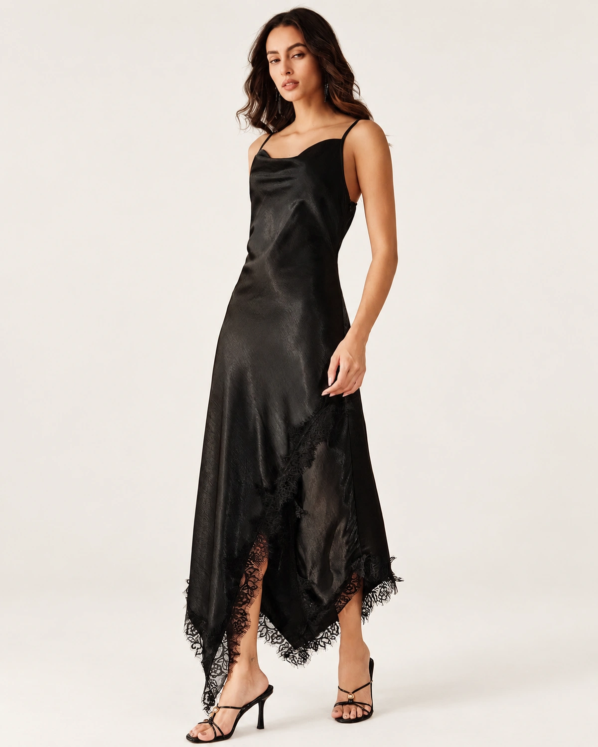 Modelo em semiperfil exibindo caimento fluido do slip dress preto acetinado com acabamento refinado.