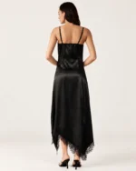 Vista posterior da modelo com vestido slip dress preto acetinado mostrando alças delicadas e decote nas costas.