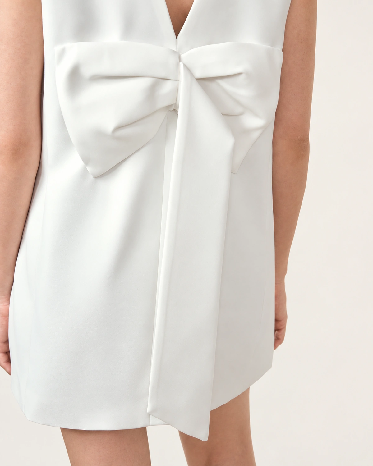 Plano médio das costas destacando o laço maximizado e acabamento de alfaiataria do vestido off-white.