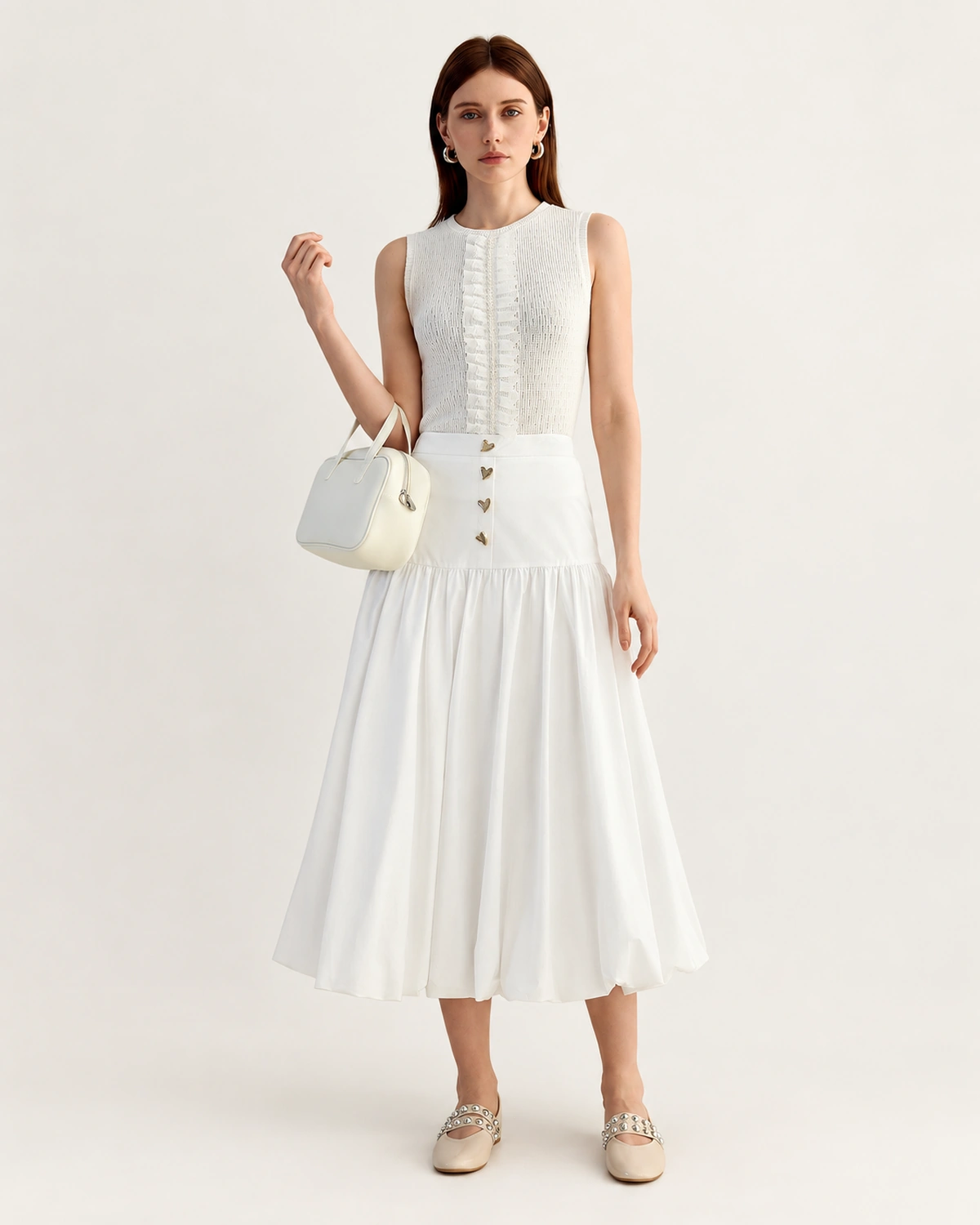 Modelo de corpo inteiro em estúdio vestindo saia midi alfaiataria plissada off-white com botões dourados e bolsa.