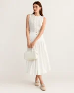 Modelo em semiperfil de corpo inteiro vestindo saia midi de alfaiataria plissada off-white.
