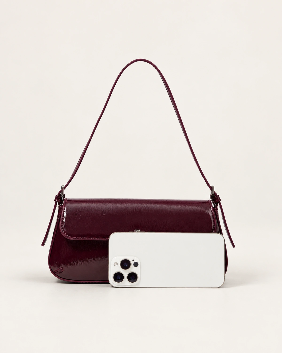 Comparativo de proporção e tamanho real da bolsa tiracolo flap bordeaux ao lado de smartphone no estúdio mineral.