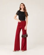 Modelo feminina de corpo inteiro em pé da cabeça aos pés com calça vermelha segurando a bolsa tiracolo flap bordeaux.