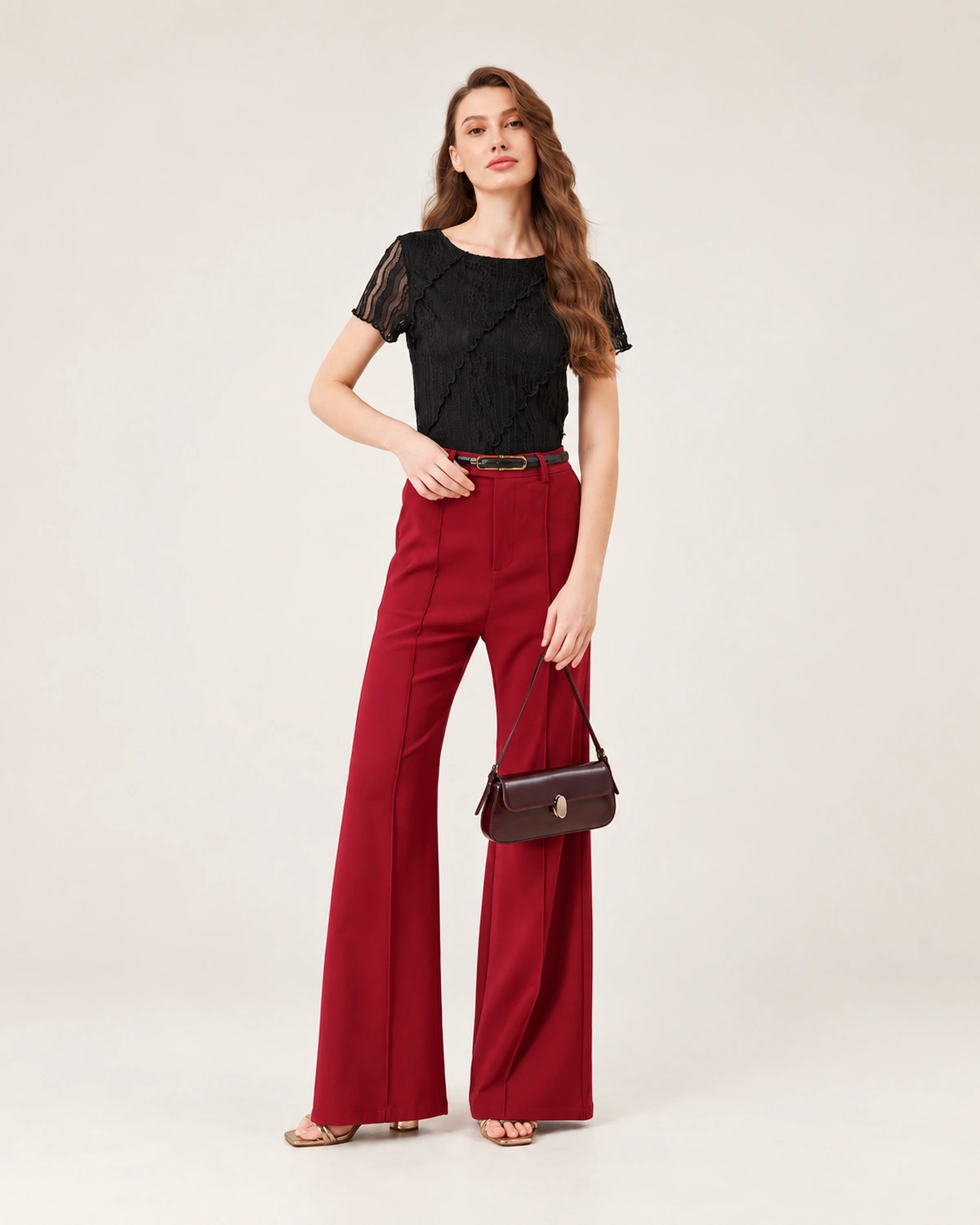 Modelo feminina de corpo inteiro em pé da cabeça aos pés com calça vermelha segurando a bolsa tiracolo flap bordeaux.