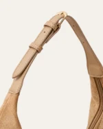 Plano detalhe da fivela metálica dourada de ajuste na alça de ombro da bolsa bucket bege areia.
