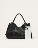 Comparativo de proporção e escala dimensional da bolsa tote preta ao lado de smartphone moderno no estúdio mineral.