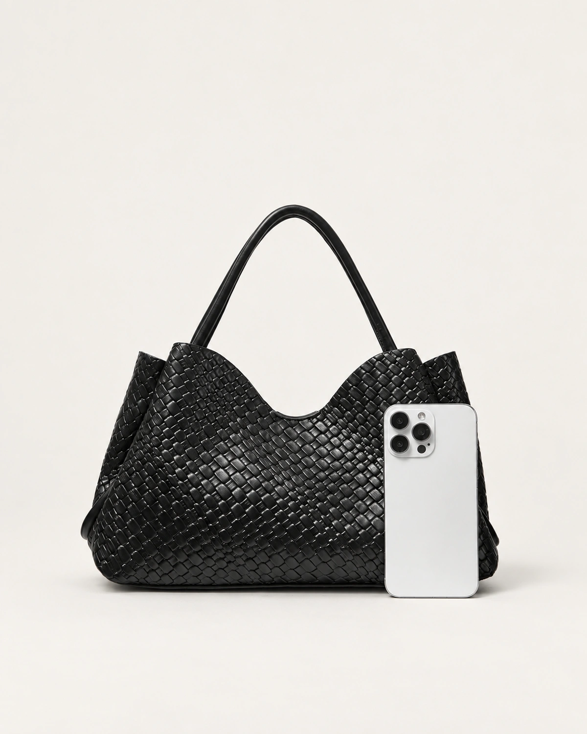 Comparativo de proporção e escala dimensional da bolsa tote preta ao lado de smartphone moderno no estúdio mineral.