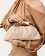 Bolsa Satchel Drapeada com Alça Escultural Metálica em tom areia com alça escultural metálica.