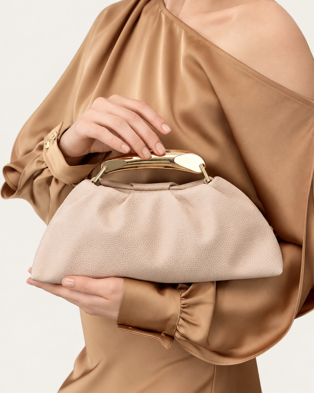 Bolsa Satchel Drapeada com Alça Escultural Metálica em tom areia com alça escultural metálica.