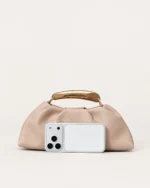 Bolsa Satchel Drapeada com Alça Escultural Metálica em tom areia com alça escultural metálica.