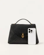 Comparativo de escala da Bolsa Satchel Estruturada preta ao lado de smartphone.