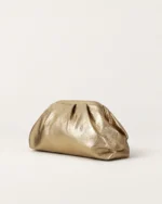Perspectiva em três quartos da bolsa clutch drapeada dourada destacando o volume orgânico e base estruturada.