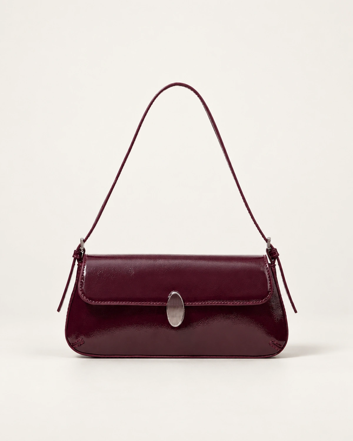 Vista frontal isolada da bolsa tiracolo flap bordeaux com fecho metálico prateado assentada no solo do estúdio mineral.