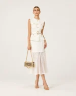 Modelo feminina de corpo inteiro da cabeça aos pés com conjunto em tweed branco e scarpins dourados segurando a bolsa tiracolo na mão.