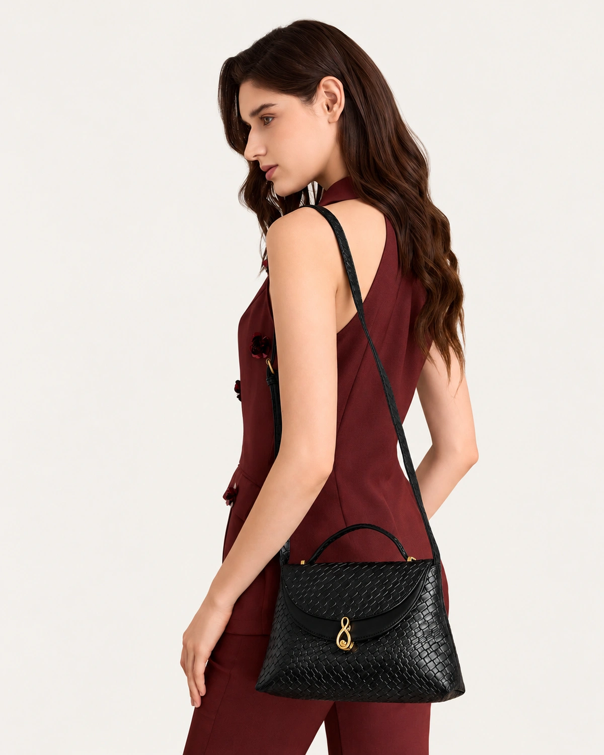 Modelo em perfil 3/4 demonstrando a Bolsa Satchel Estruturada Tressê preta no quadril.