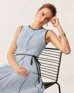 Modelo sentada vestindo colete e saia Azul Céu com vivos pretos.