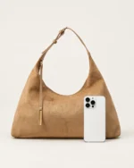 Comparativo de escala e tamanho real da bolsa bucket bege areia ao lado de smartphone no estúdio mineral.