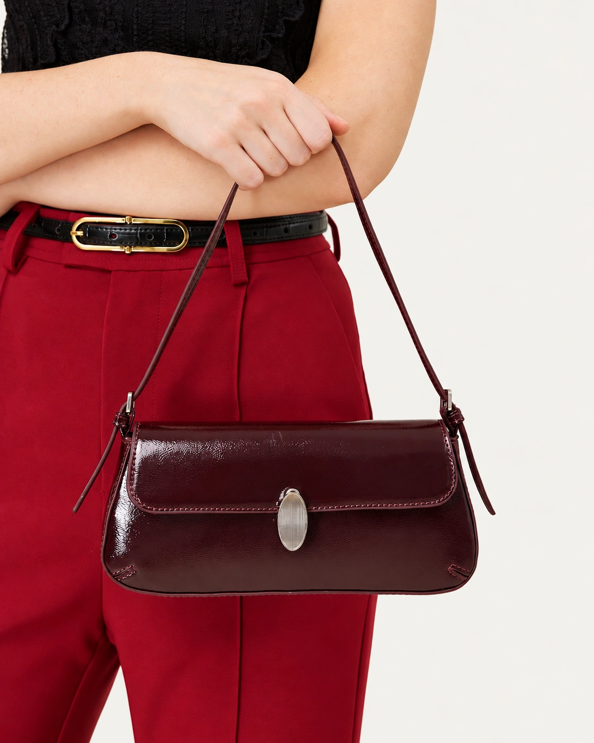 Plano detalhe na altura do quadril destacando a mão da modelo na alça da bolsa tiracolo bordeaux contra calça vermelha.