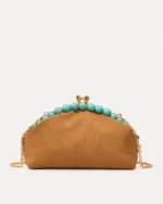 Bolsa clutch marrom com alça de corrente dourada estendida sobre fundo mineral neutro