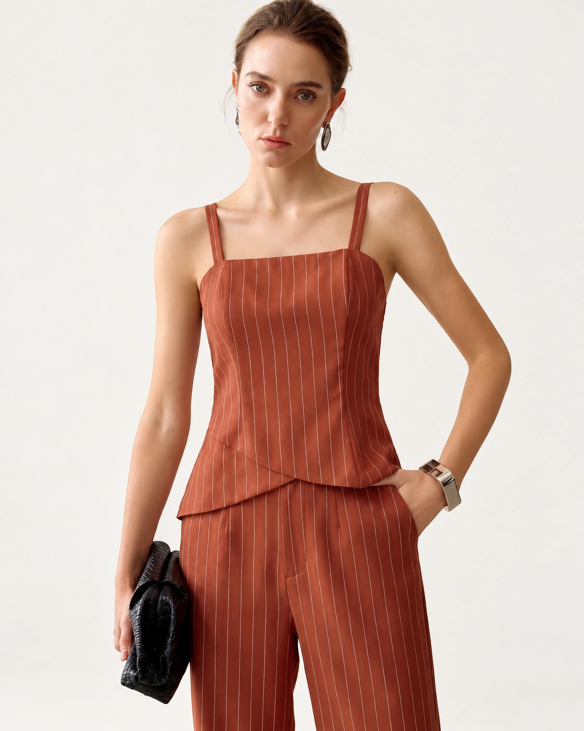 Modelo em plano americano com conjunto de alfaiataria risca de giz terracota e clutch de mão.