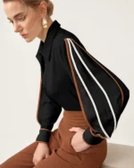 Modelo sentada de perfil vestindo camisa preta com vivos contrastantes e calça pantalona marrom