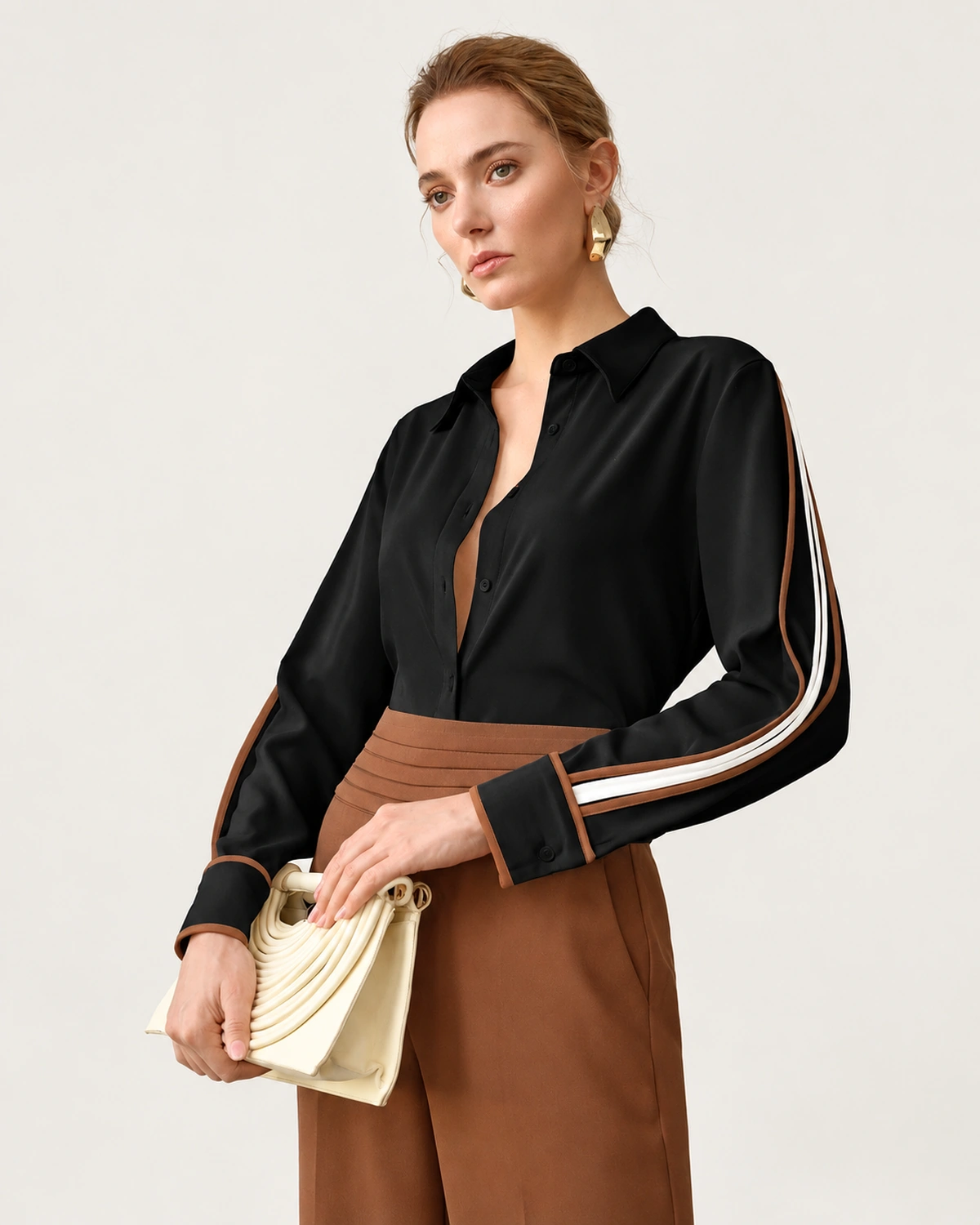 Plano médio da modelo segurando clutch marfim vestindo camisa preta clássica com vivos contrastantes