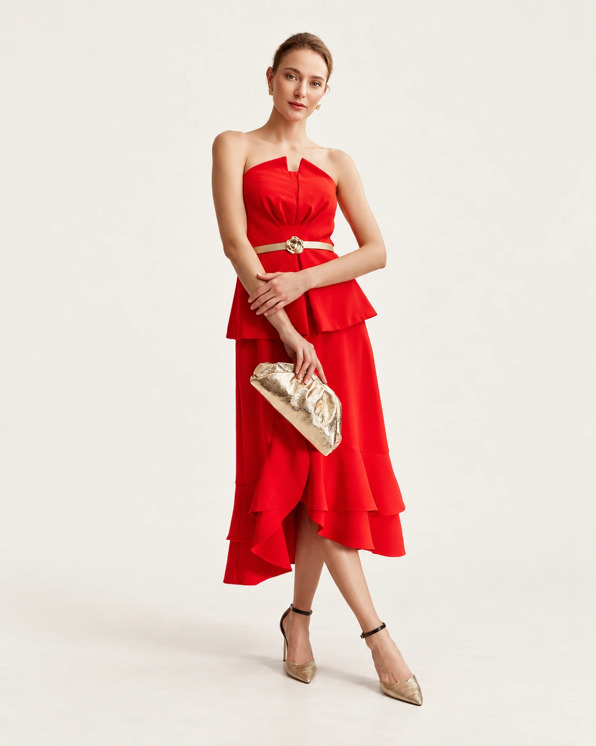 Modelo feminina de corpo inteiro da cabeça aos pés com vestido midi vermelho e scarpins dourados segurando a clutch na mão.
