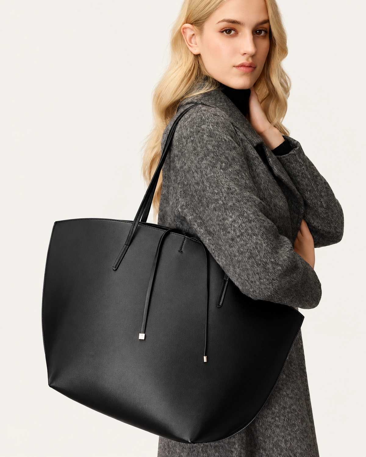 Modelo feminina em plano médio com sobretudo de lã cinza segurando a bolsa tote ampla preta no ombro.