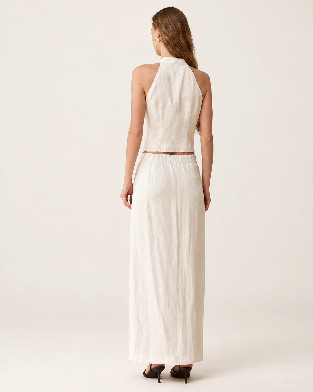 Vista de costas da modelo vestindo colete halter e saia midi em linho off-white.
