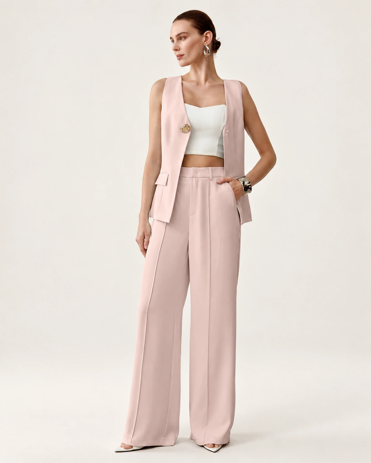 Modelo feminina vestindo conjunto de alfaiataria rosa blush com colete decote V e calça pantalona em estúdio mineral