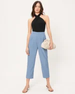 Modelo de corpo inteiro vestindo regata preta ajustada com decote halter cruzado e calça de alfaiataria.