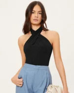 Modelo em plano médio frontal segurando clutch e exibindo regata halter preta ajustada.