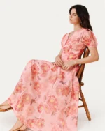 Modelo sentada em cadeira de madeira vestindo vestido midi floral rosa blush com mangas bufantes