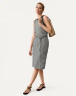 Modelo em movimento de passo com vestido midi listrado preto e branco e bolsa