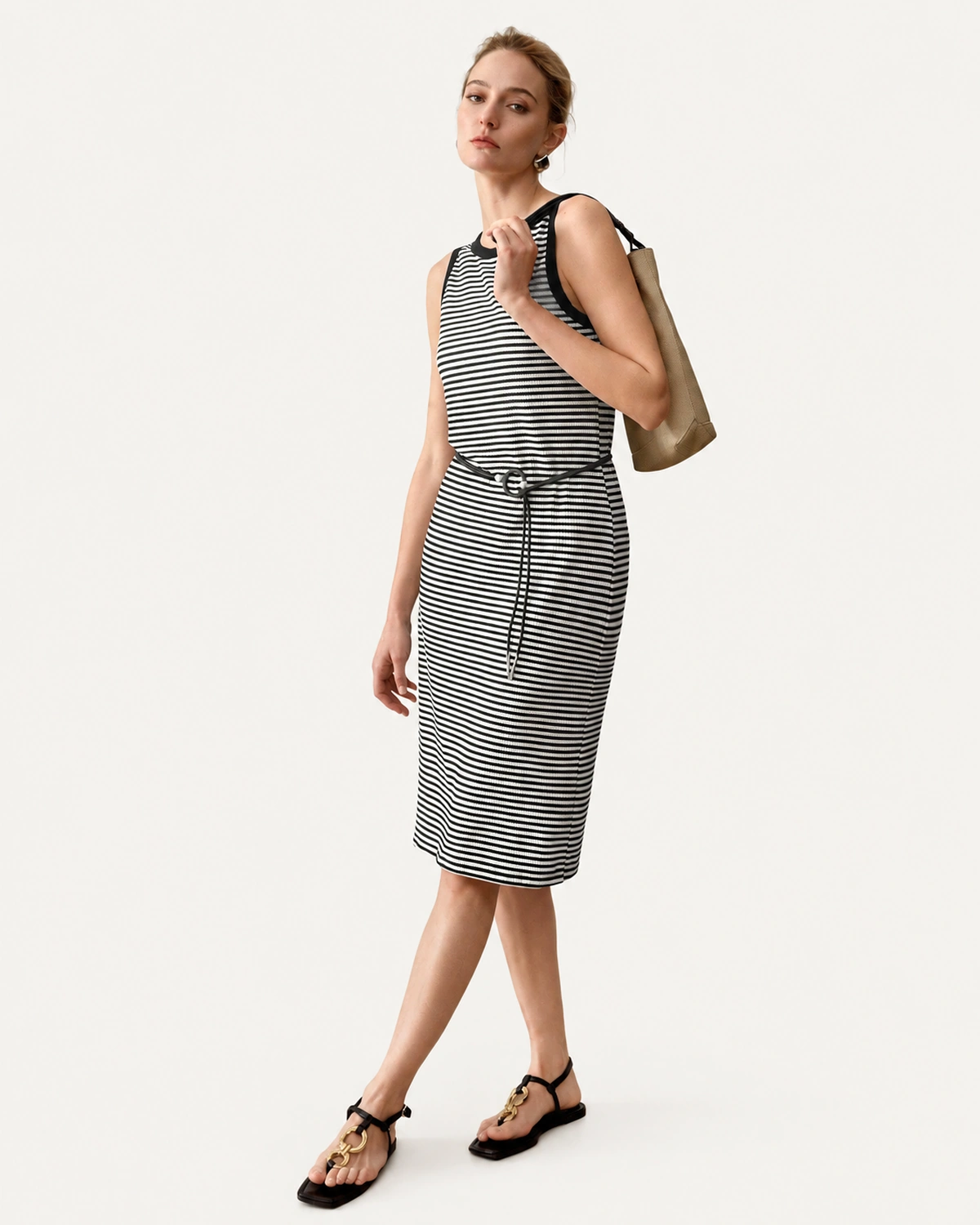 Modelo em movimento de passo com vestido midi listrado preto e branco e bolsa