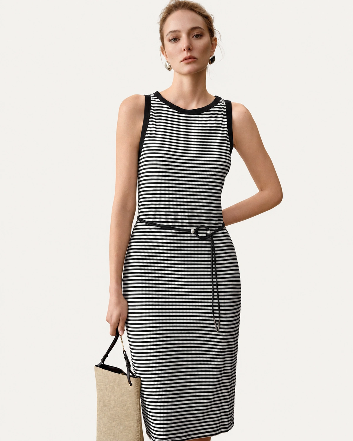 Plano médio da modelo vestindo vestido midi listrado preto e branco com cinto fino e bolsa