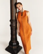 Editorial sofisticado com modelo apoiada na coluna exibindo o caimento do vestido na cor Terracota Solar.