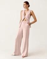 Modelo feminina de corpo inteiro vestindo conjunto de alfaiataria rosa blush com calça fluida em estúdio mineral