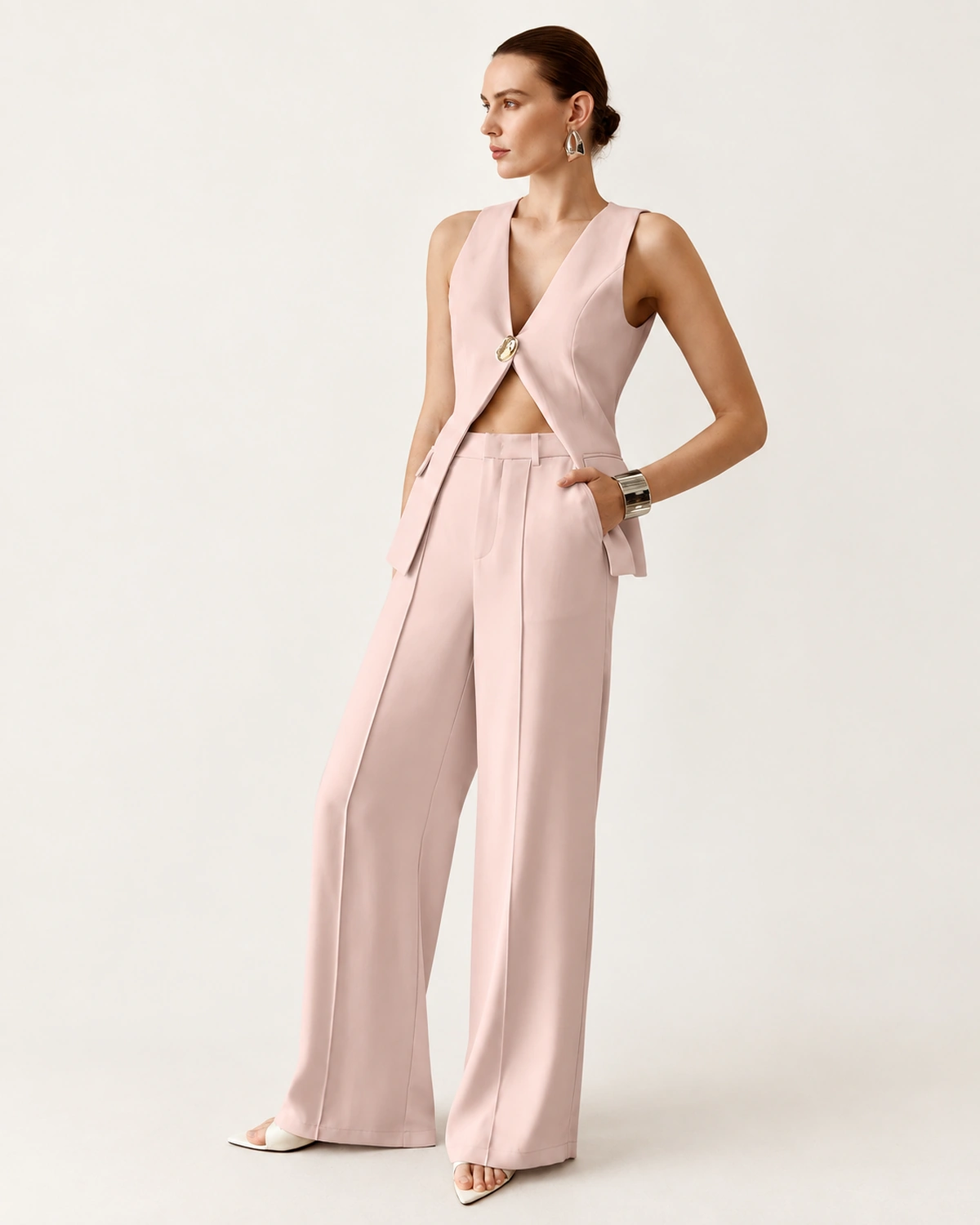 Modelo feminina de corpo inteiro vestindo conjunto de alfaiataria rosa blush com calça fluida em estúdio mineral