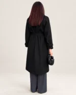 Modelo de costas em plano de corpo inteiro com sobretudo preto alongado com cinto e calça pantalona cinza