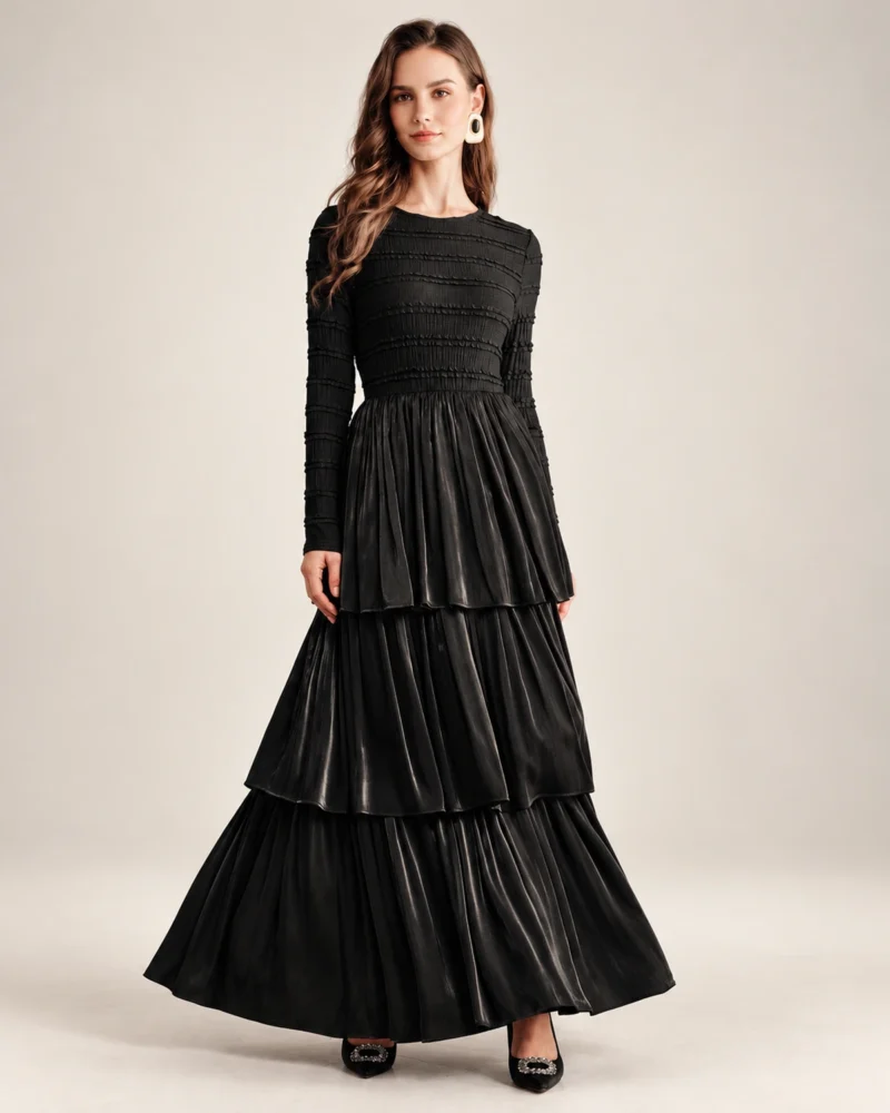 Modelo vestindo vestido longo preto acetinado com saia em três camadas plissadas em estúdio mineral