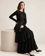 Modelo vestindo vestido longo preto acetinado com saia em três camadas plissadas em estúdio mineral