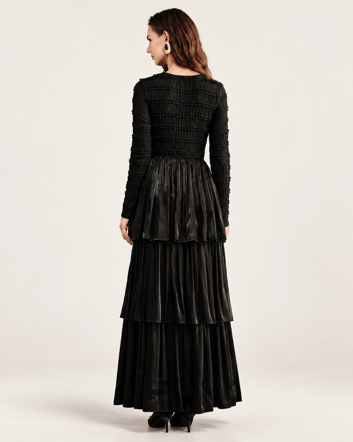 Modelo vestindo vestido longo preto acetinado com saia em três camadas plissadas em estúdio mineral