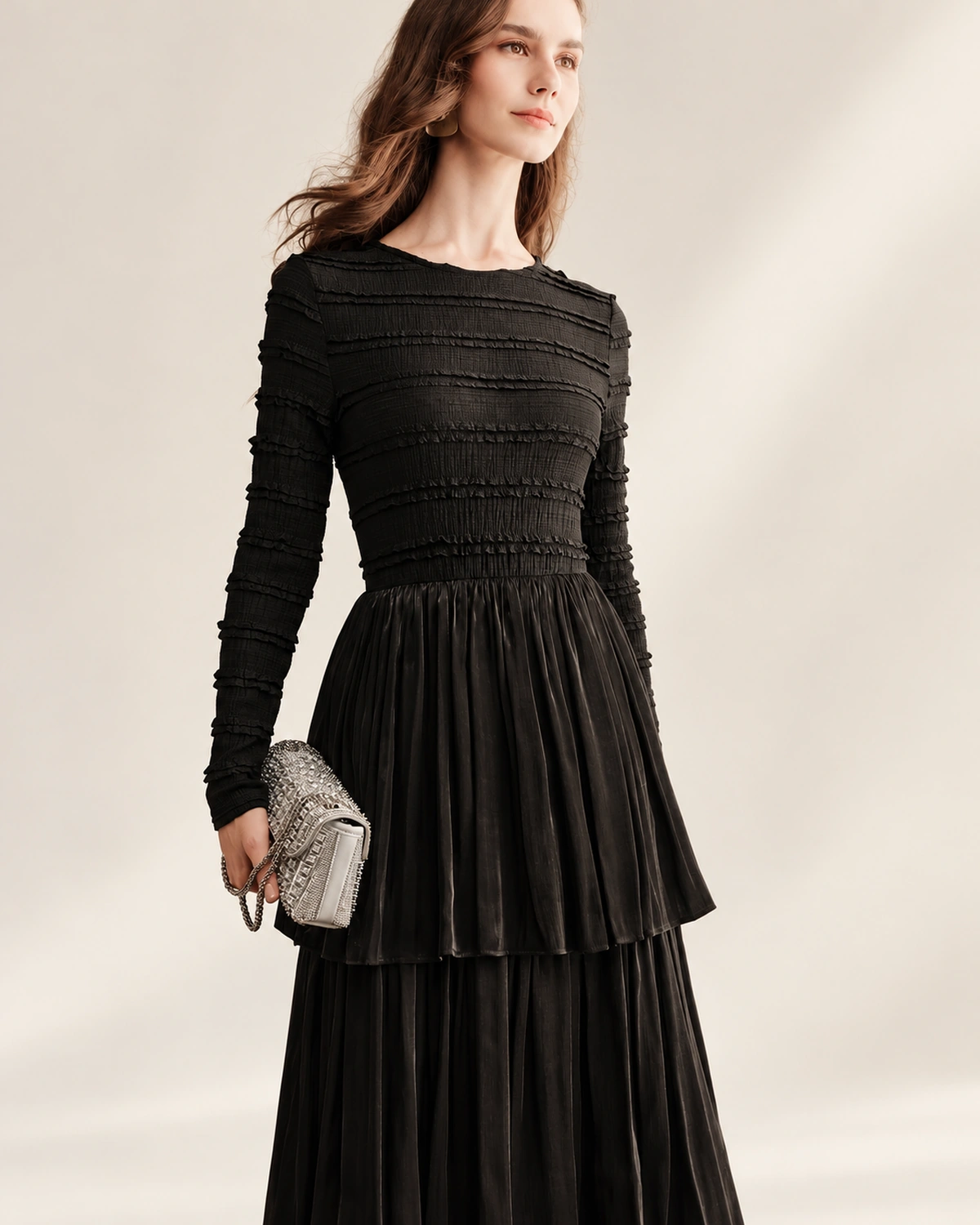 Modelo vestindo vestido longo preto acetinado com saia em três camadas plissadas em estúdio mineral