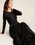 Modelo vestindo vestido longo preto acetinado com saia em três camadas plissadas em estúdio mineral