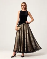 Plano frontal da modelo vestindo vestido longo de veludo e saia em renda sobre forro champanhe em estúdio mineral.