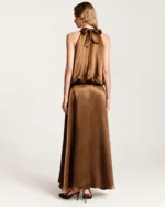 Vista posterior da modelo vestindo vestido em cetim bronze com laço na nuca em estúdio mineral