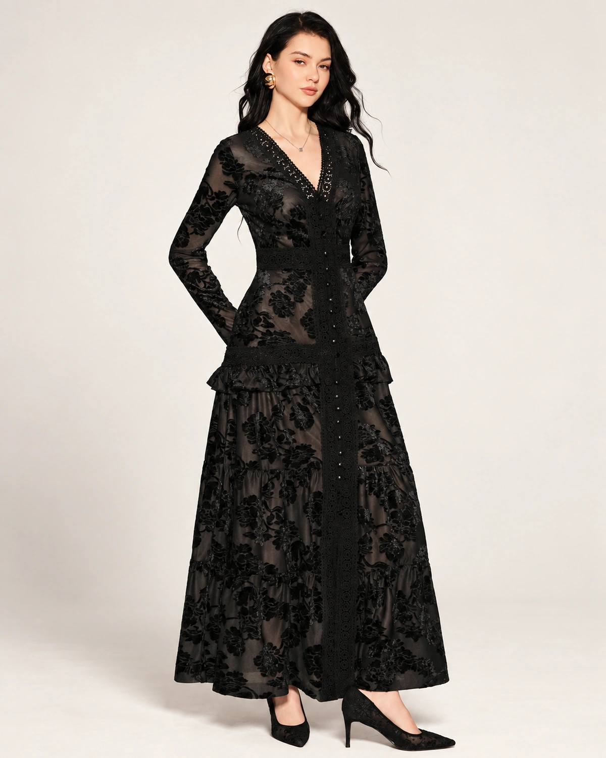 Plano médio da modelo com vestido longo em renda devorê preta destacando mangas longas e decote V