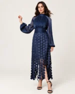 Vestido longo em tule com gola alta franzida, mangas fluidas e saia com aplicações circulares na cor azul-marinho, vista frontal.